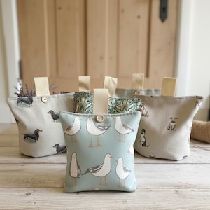 May include: A collection of four fabric doorstops with handles and wooden buttons. One features a light blue background with white seagulls, another has a beige background with various dog breeds, and one displays a green and white botanical pattern.