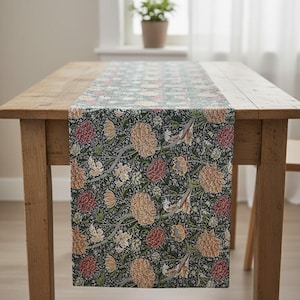 May include: A patterned table runner with a floral design in green, red, and gold. It is placed on a wooden table. The runner's botanical pattern includes detailed flowers and leaves, enhancing the dining table's aesthetic appeal.
