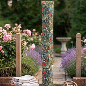 May include: A tall, cylindrical fabric draught excluder featuring a vibrant floral print with red poppies, blue cornflowers, and white daisies on a green background. The item stands vertically, showcasing a detailed botanical pattern across its surface.