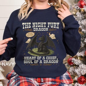 Puede incluir: Sudadera azul marino con una ilustraci&oacute;n de un drag&oacute;n negro y el texto "THE NIGHT FURY DRAGON". El dise&ntilde;o incluye las frases "Warning Never Engage This Dragon" y "HEART OF A CHIEF, SOUL OF A DRAGON."