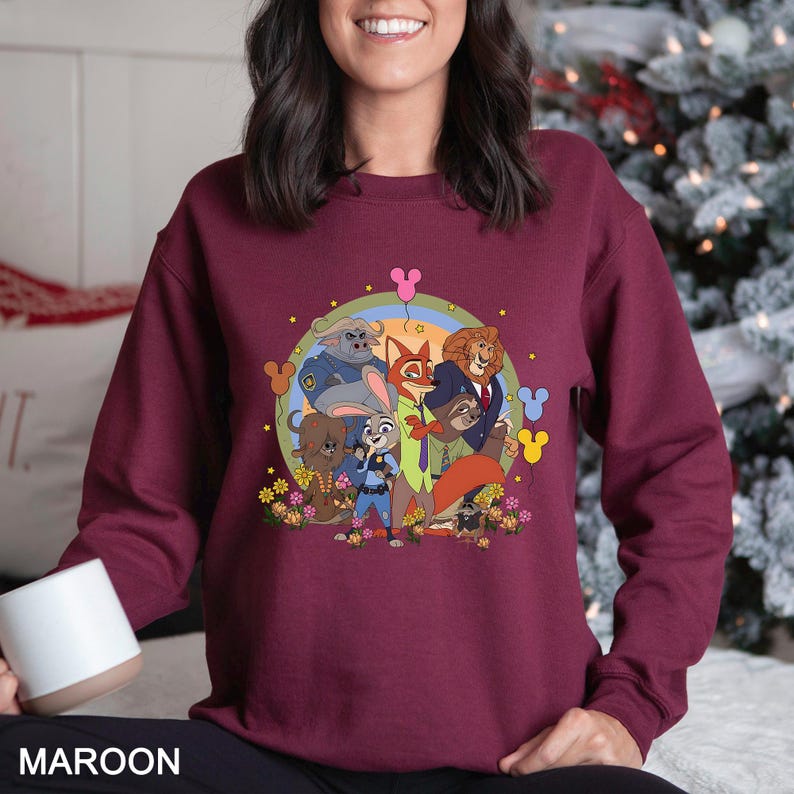May include: Maroon sweatshirt featuring a colorful graphic of cartoon animal characters. The design includes a rainbow, flowers, and Mickey Mouse-shaped balloons. The word "MAROON" is printed at the bottom of the sweatshirt.