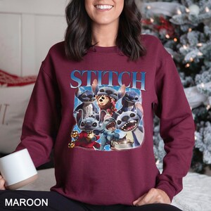Op de afbeelding: Bordeaux sweatshirt met een afbeelding van het personage Stitch uit de Disney-film Lilo & Stitch. Het woord "STITCH" is in blauw boven de afbeelding gedrukt. De sweatshirt heeft een effen bordeauxrode kleur.