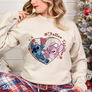 May include: A cream-colored sweatshirt with a graphic of Stitch and Angel from Lilo & Stitch. The graphic is a heart with stars and the text "Better Together".