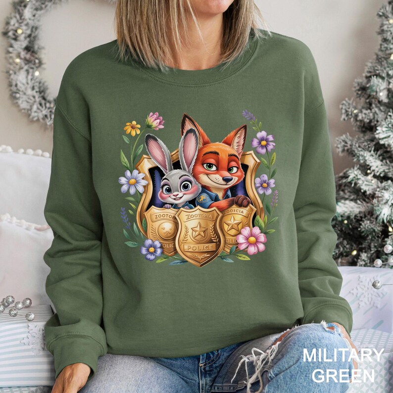 Puede incluir: Sudadera verde oliva con un gr&aacute;fico colorido de Judy Hopps y Nick Wilde de Zootopia, enmarcado por flores y placas de polic&iacute;a. El dise&ntilde;o incluye el texto "Zootopia Police". La sudadera es de estilo casual y c&oacute;modo.