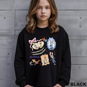 May include: Black crewneck sweatshirt featuring colorful cartoon images from the movie "Zootopia." The design includes characters in ornate frames, a pink bow, and the word "Zootopia." The sweatshirt is made of a soft material.
