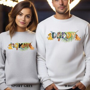 May include: Sport grey and white sweatshirts with the words "MOMMY" and "DADDY" in colorful letters, featuring cartoon lion characters and tropical leaves. The sweatshirts are a matching set.