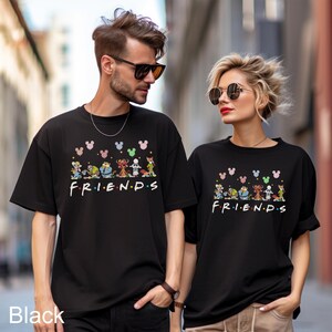 May include: Black t-shirts with the word "FRIENDS" in the style of the TV show logo, with cartoon characters and Mickey Mouse heads above the word. The t-shirts are worn by two people.
