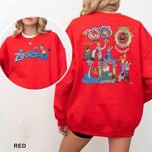 K&ouml;nnte beinhalten: Rotes Sweatshirt mit dem Wort "Zootopia" in Blau und einer Cartoon-Grafik auf der Vorderseite. Auf der R&uuml;ckseite des Sweatshirts befindet sich eine farbenfrohe Grafik von Charakteren aus dem Animationsfilm "Zootopia".
