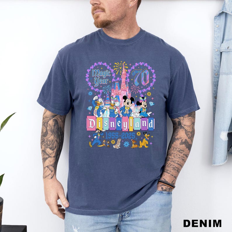 May include: A navy blue t-shirt featuring a colorful Disneyland graphic. The design includes Mickey and Minnie Mouse, Donald Duck, and other Disney characters, along with the text "Magic Year 70 Disneyland 1955-2025".
