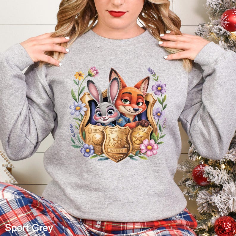 Puede incluir: Una sudadera gris claro con un gr&aacute;fico colorido de Judy Hopps y Nick Wilde de Zootopia, enmarcado por flores y placas de polic&iacute;a. El texto "Sport Grey" est&aacute; en la parte inferior de la imagen.
