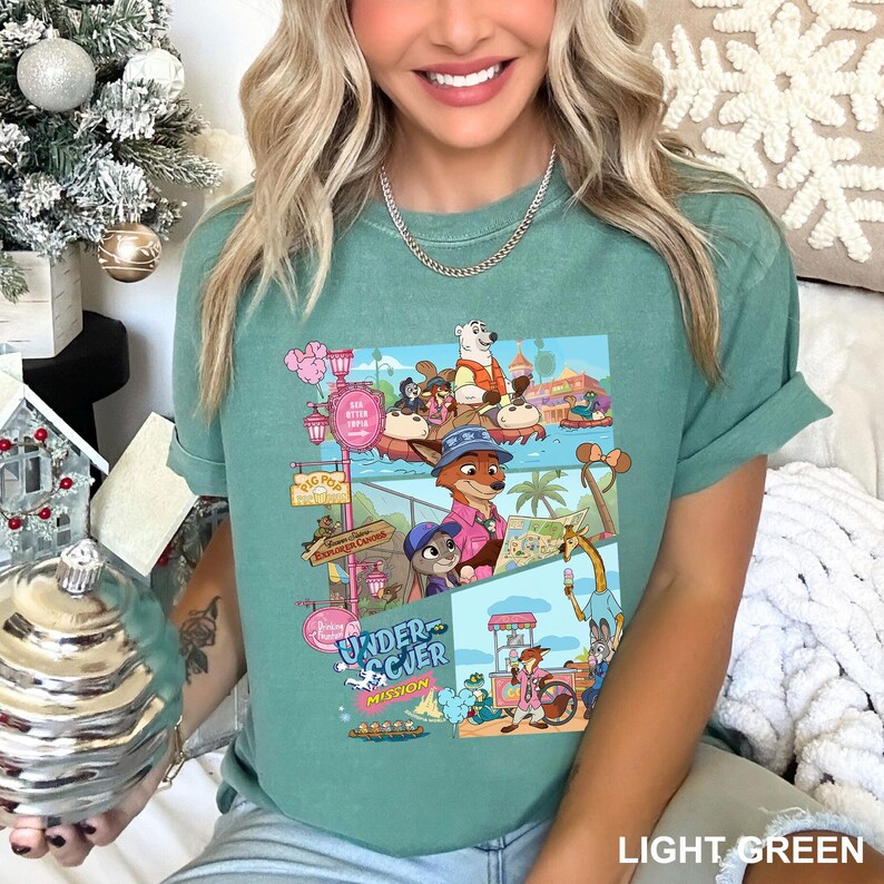 May include: Light green t-shirt with a vibrant graphic of animated characters and the text "Undercover Mission." The design includes various scenes with animals and the words "Big Pop" and "Explorer Canoes."