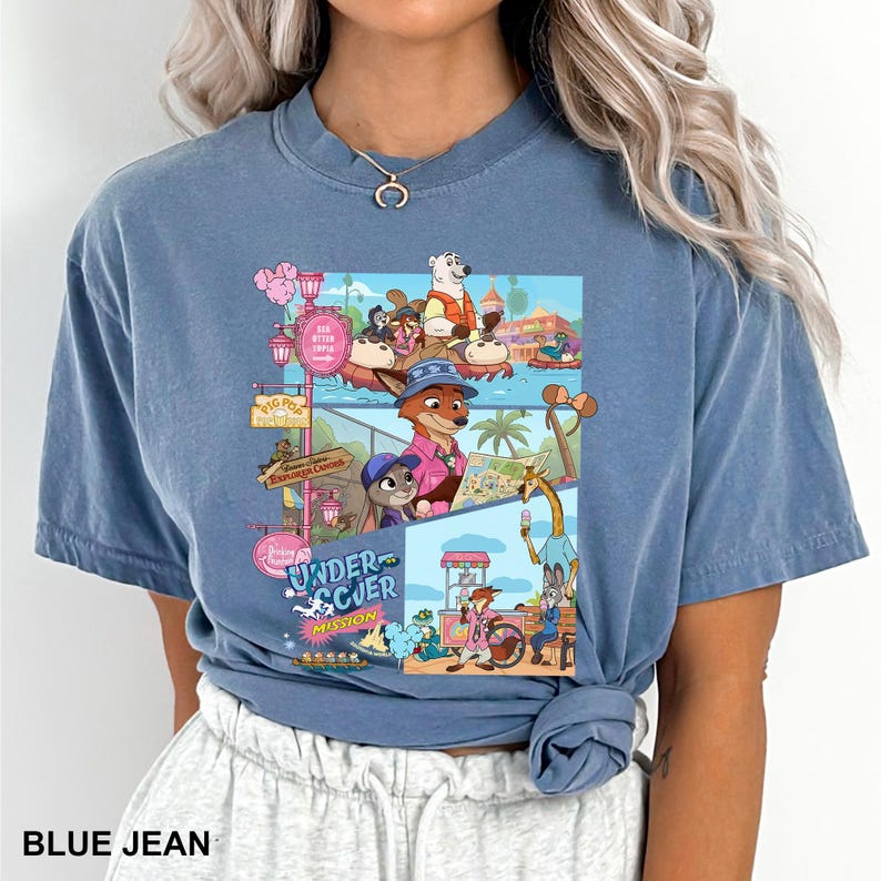 May include: Blue jean coloured t-shirt with a vibrant graphic from the animated film Zootopia. The design showcases characters such as Nick Wilde and Judy Hopps in a theme park scene. The text "UNDER SCUER MISSION" is also displayed.
