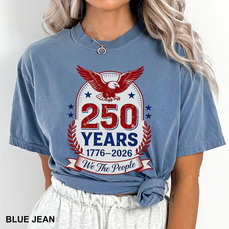 May include: A blue jean colored t-shirt with a graphic commemorating 250 years, from 1776 to 2026. The design features a red eagle, stars, and the text "We The People."