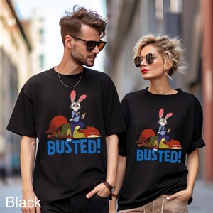 May include: Black t-shirts featuring a cartoon image of a rabbit police officer on top of a fox, with the word "BUSTED!" in blue. The t-shirts are worn by two people, one male and one female.