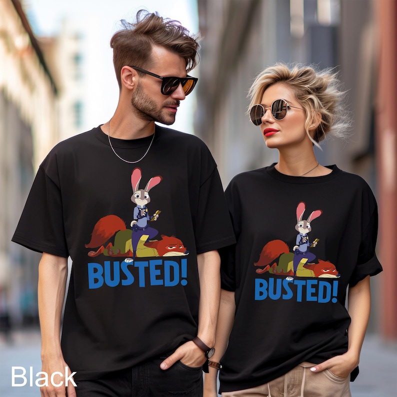 May include: Black t-shirts featuring a cartoon image of a rabbit police officer on top of a fox, with the word "BUSTED!" in blue. The t-shirts are worn by two people, one male and one female.