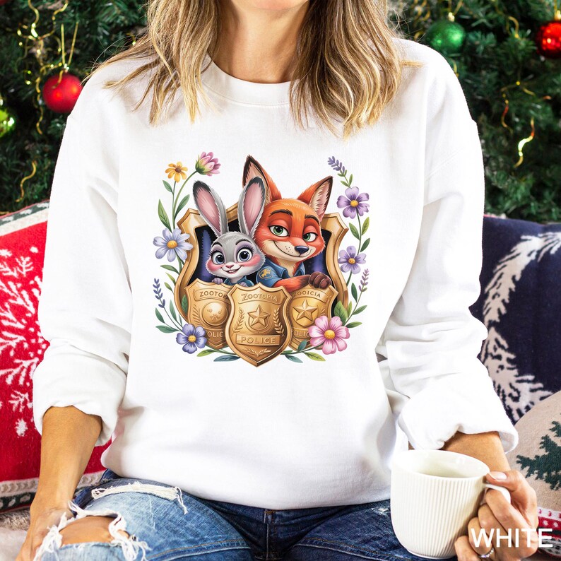 Puede incluir: Sudadera blanca con un gr&aacute;fico colorido de Judy Hopps y Nick Wilde de Zootopia, enmarcado por flores y placas de polic&iacute;a. La sudadera tiene mangas largas y cuello redondo. La palabra "WHITE" est&aacute; impresa en la parte inferior derecha.