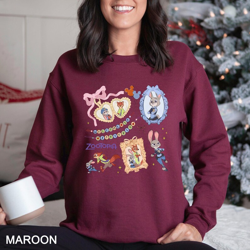 May include: Maroon sweatshirt featuring multiple framed images of characters from the animated film Zootopia. The sweatshirt has a crew neck and long sleeves. The word "Zootopia" is printed in white script below the images.