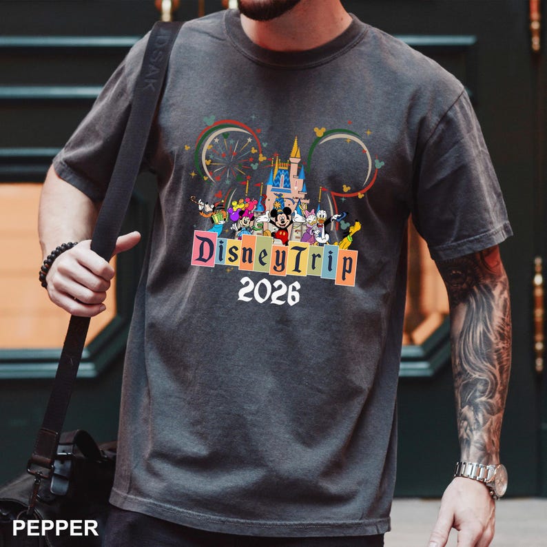 May include: Dark gray t-shirt featuring a colorful Disney Trip design with Mickey Mouse and friends, a castle, and the text "Disney Trip 2026". The design includes a rainbow and a Ferris wheel.