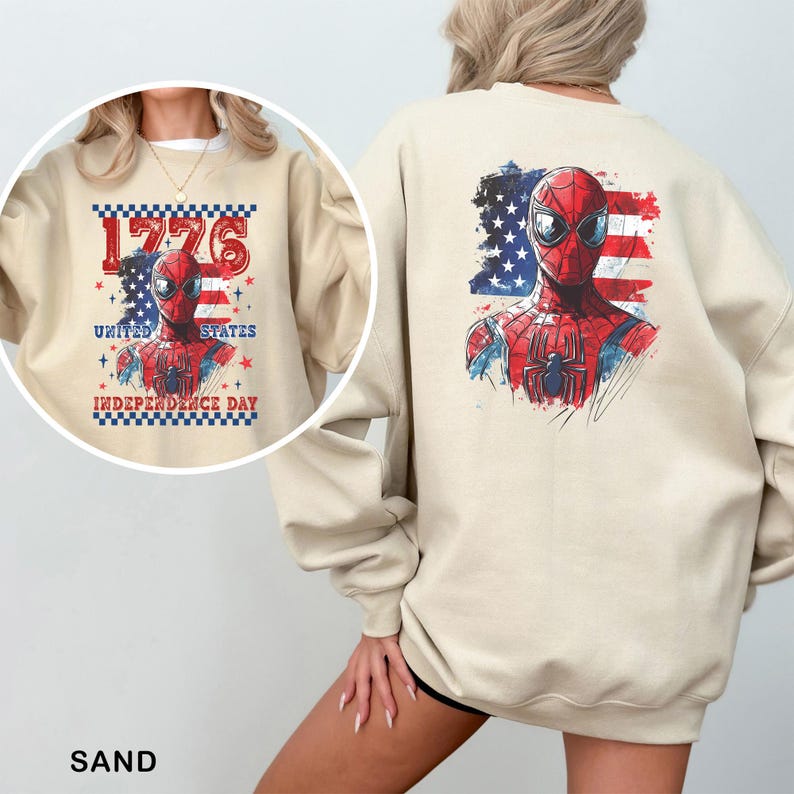 May include: A sand-coloured crewneck sweatshirt featuring a graphic of Spider-Man against a distressed American flag. The back displays a large print, while the circular inset shows a front design with the text 1776 UNITED STATES INDEPENDENCE DAY.