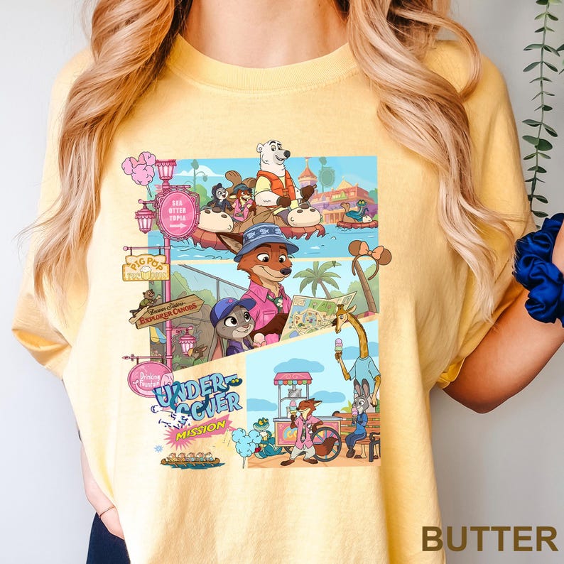 May include: Yellow t-shirt with a vibrant graphic of cartoon animals in a theme park. The design includes a fox, a bunny, and a giraffe, with the word "BUTTER" printed at the bottom of the shirt.
