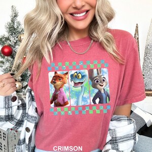 May include: Crimson-colored t-shirt featuring a graphic of three animated characters: a fox, a snake, and a rabbit. The graphic is framed with a green and blue checkered pattern. The word "CRIMSON" is printed at the bottom of the shirt.