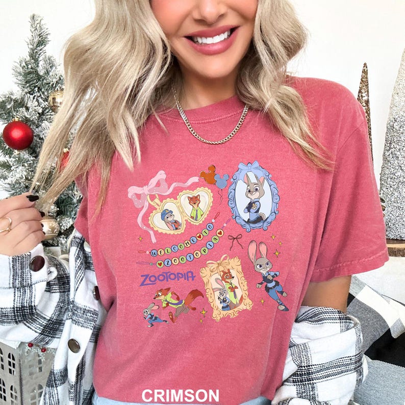 May include: Crimson-colored t-shirt featuring Zootopia characters in framed illustrations. The shirt has a crew neck and short sleeves. The word "Zootopia" is printed in a stylized font below the illustrations.