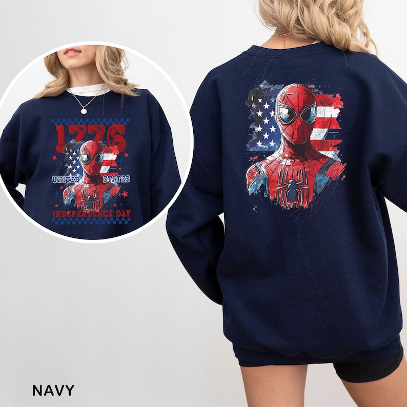 May include: A navy blue crewneck sweatshirt featuring a graphic of a red and blue superhero mask over a distressed American flag. The front design includes the text 1776, UNITED STATES, and INDEPENDENCE DAY in red and blue lettering.