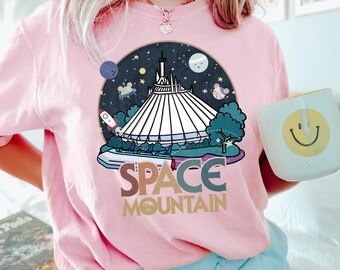 May include: Pink t-shirt with a graphic of Space Mountain, a roller coaster ride at Disney World. The graphic is surrounded by stars and planets. The text "Space Mountain" is written in a retro font.