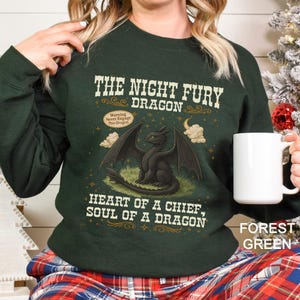 Puede incluir: Sudadera verde bosque con un gr&aacute;fico de un drag&oacute;n negro, el texto "THE NIGHT FURY DRAGON" y la frase "HEART OF A CHIEF, SOUL OF A DRAGON". La sudadera tambi&eacute;n tiene el texto "Warning Never Engage This Dragon".