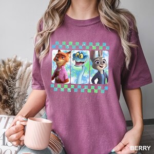 May include: Berry-colored t-shirt featuring a graphic of three animated characters: a fox, a snake, and a rabbit. The graphic is framed with a checkered pattern in blue and green. The word "BERRY" is printed at the bottom right.