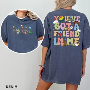 May include: Denim blue t-shirt with a Toy Story character graphic on the front and the text "YOU'VE GOT A FRIEND IN ME" on the back. The shirt has a relaxed fit and short sleeves, suitable for everyday wear.