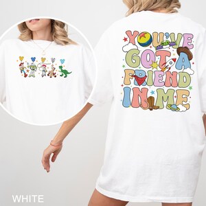 May include: White t-shirt with a colourful Toy Story design, including characters and the text "You've Got A Friend In Me." The graphic features a cowboy hat, rocket, and other playful elements. The shirt has a relaxed fit.