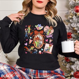 Puede incluir: Sudadera negra de cuello redondo con un gr&aacute;fico colorido de personajes de Zootopia, incluyendo a Nick Wilde y Judy Hopps. El dise&ntilde;o incluye las palabras "Best Friends Forever" y "Bestie". La palabra "BLACK" est&aacute; impresa en la parte inferior.