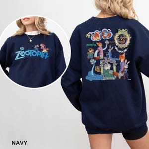 K&ouml;nnte beinhalten: Marineblaues Sweatshirt mit dem Wort "Zootopia" in teal auf der Vorderseite gestickt. Auf der R&uuml;ckseite befindet sich eine farbenfrohe Grafik von Charakteren aus dem Animationsfilm "Zootopia".