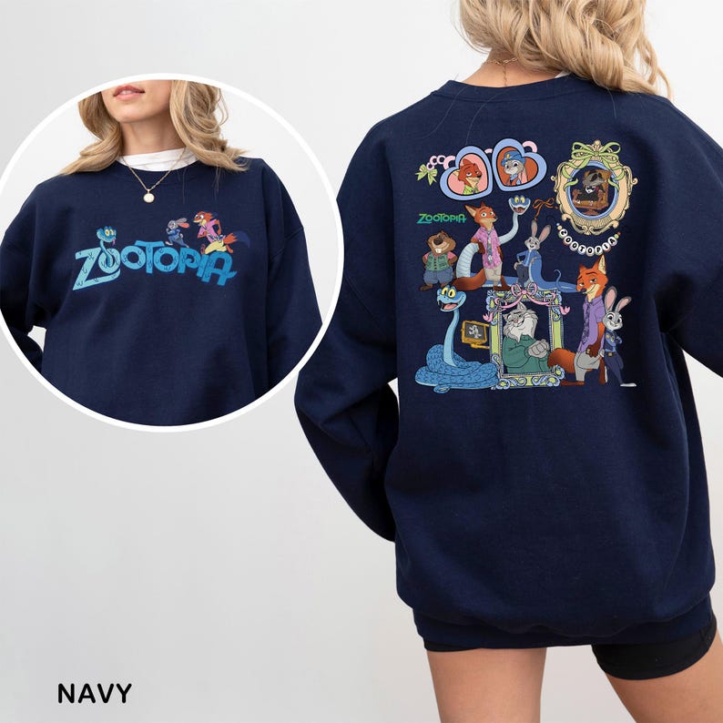 K&ouml;nnte beinhalten: Marineblaues Sweatshirt mit dem Wort "Zootopia" in teal auf der Vorderseite gestickt. Auf der R&uuml;ckseite befindet sich eine farbenfrohe Grafik von Charakteren aus dem Animationsfilm "Zootopia".