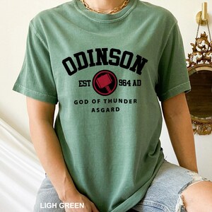 May include: A light green t-shirt with the text "ODINSON EST 964 AD GOD OF THUNDER ASGARD" and a red and black hammer graphic.
