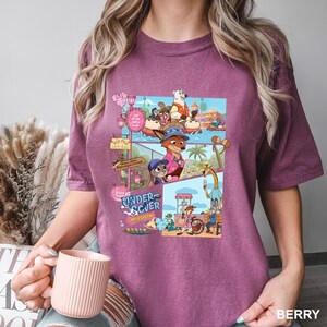 May include: Berry-coloured t-shirt with a colourful graphic from the animated film Zootropolis. The graphic includes the words "Undercover Mission" and various cartoon characters in a tropical setting.