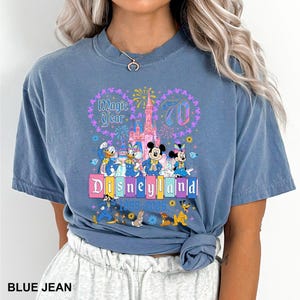 May include: Blue jean t-shirt featuring a Disneyland 70th anniversary design. The graphic includes Mickey and Minnie Mouse, Donald and Daisy Duck, and the Disneyland castle. The text "Magic Year" and "Disneyland 1955-2025" are also visible.