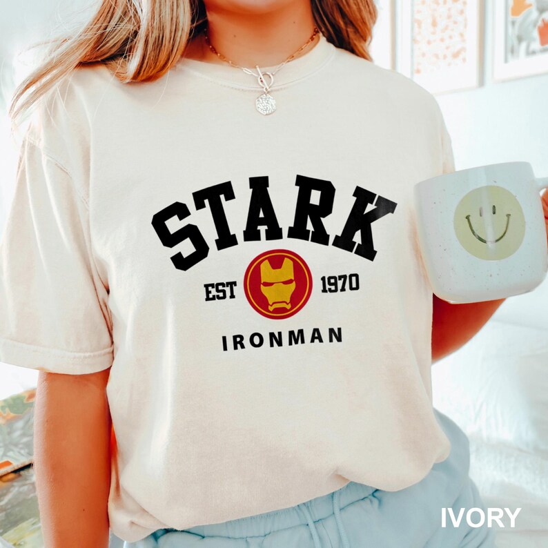 May include: White t-shirt with black text that reads "STARK EST 1970 IRONMAN" and a red and yellow Iron Man mask graphic.