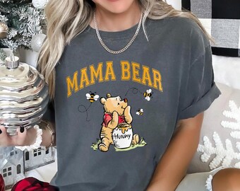 May include: A gray t-shirt with the text "Mama Bear" in yellow letters. A cartoon Winnie the Pooh bear is holding a pot of honey with bees flying around him.