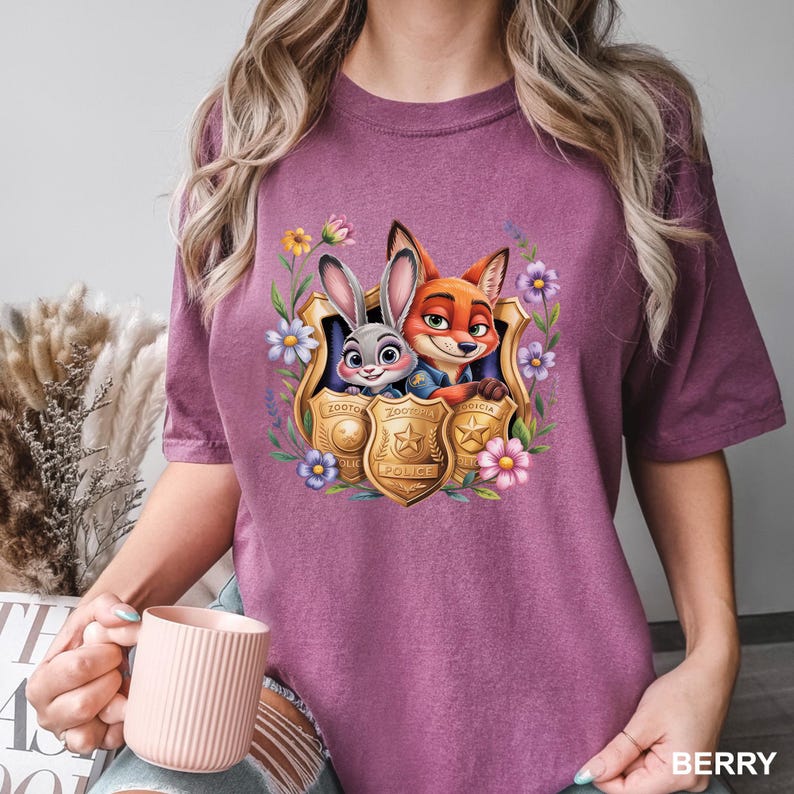 May include: Berry-coloured t-shirt featuring a graphic of Judy Hopps and Nick Wilde from Zootopia, framed by a floral design. The characters are inside police badge emblems. The word "BERRY" is printed at the bottom right.