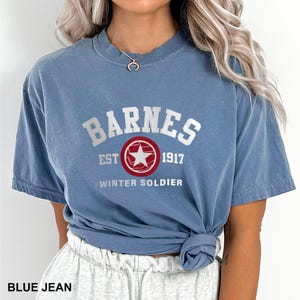 May include: A blue jean t-shirt with white text that reads "Barnes Est 1917 Winter Soldier" and a red circle with a white star in the center.
