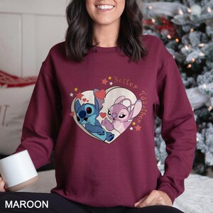May include: A maroon sweatshirt with a heart-shaped design featuring two cartoon characters, Stitch and Angel, with the text "Better Together" above them.