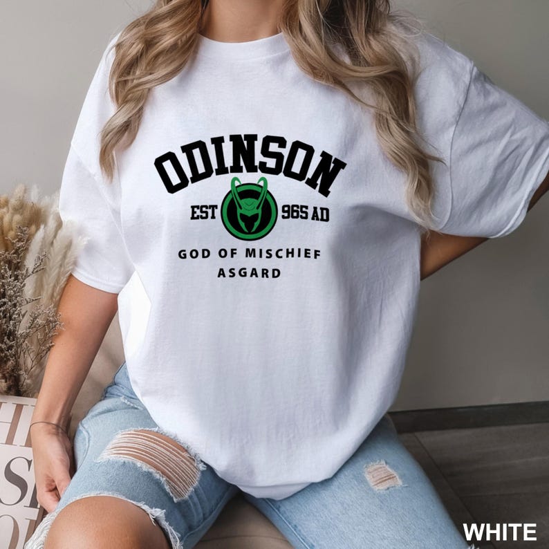 May include: White t-shirt with black text that reads "ODINSON EST 965 AD GOD OF MISCHIEF ASGARD" and a green and black logo of a horned helmet.