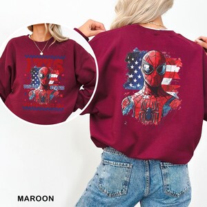 May include: A maroon long-sleeve sweatshirt featuring a graphic of Spider-Man against a distressed American flag background. The front design includes the text 1776 UNITED STATES INDEPENDENCE DAY. The back displays a larger version of the same graphic.