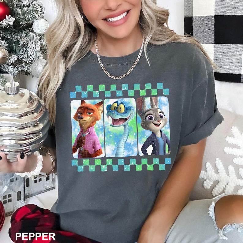May include: Dark gray t-shirt featuring a graphic of three cartoon characters in a checkered frame. The characters are a fox in a pink shirt, a snake, and a rabbit in a blue jacket. The word "PEPPER" is printed at the bottom.