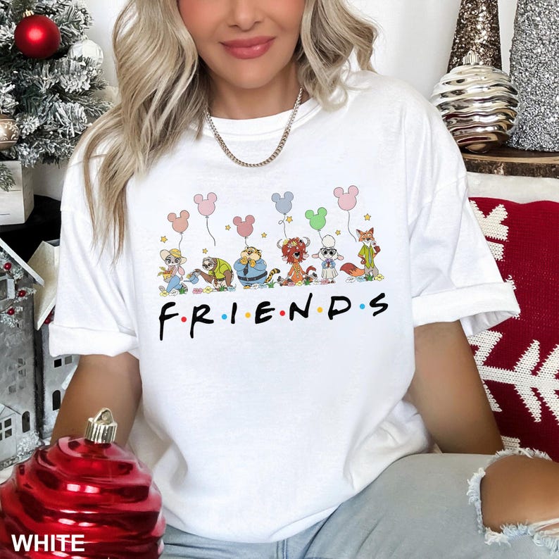 May include: White t-shirt with a cartoon graphic of characters holding balloons, each with Mickey Mouse ears. The word "FRIENDS" is printed in black. The shirt is a casual style, suitable for everyday wear.