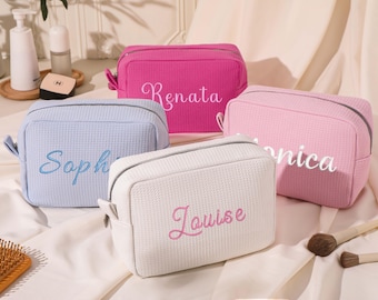 May include: Four zippered cosmetic bags in different colours with personalised names embroidered on them. The bags are light blue, white, pink, and hot pink. The names are "Sophia", "Louise", "Monica", and "Renata".