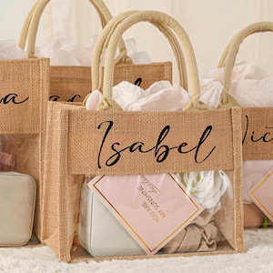 May include: Three burlap gift bags with clear plastic windows. The bags are personalized with the names "Isla", "Isabel", and "Victoria". Each bag contains a small gift box and a card.