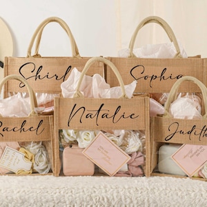 Könnte beinhalten: Fünf Tragetaschen aus Jute, personalisiert mit Namen in eleganter Schrift: Shirley, Sophia, Natalie, Rachel und Judith. Die Taschen haben transparente Fronten und sind mit Geschenken und Dekorationen gefüllt.